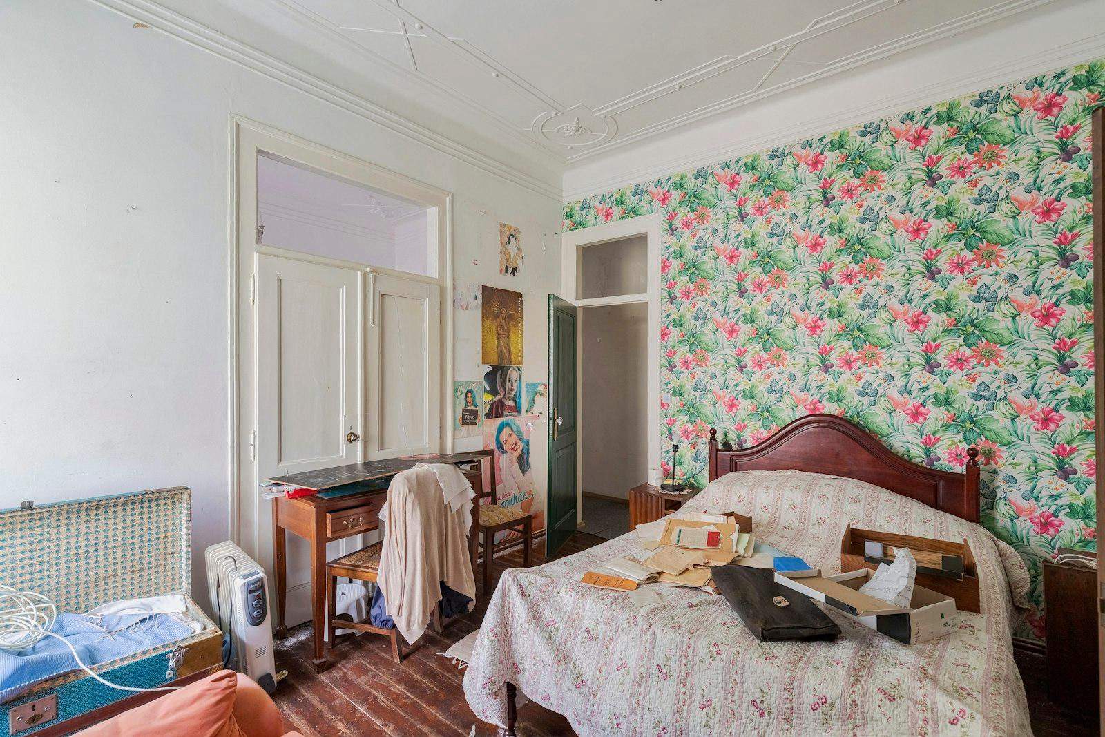 An old bedroom with floral wallpaper and belongings left out
